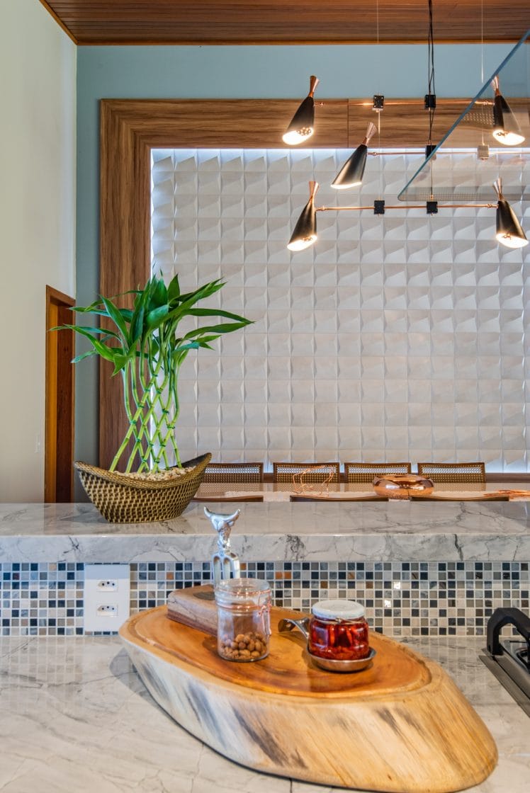Sala de jantar iluminada com destaque para a cerâmica da parede e balcão de pedra com pastilhas em tons de azul.