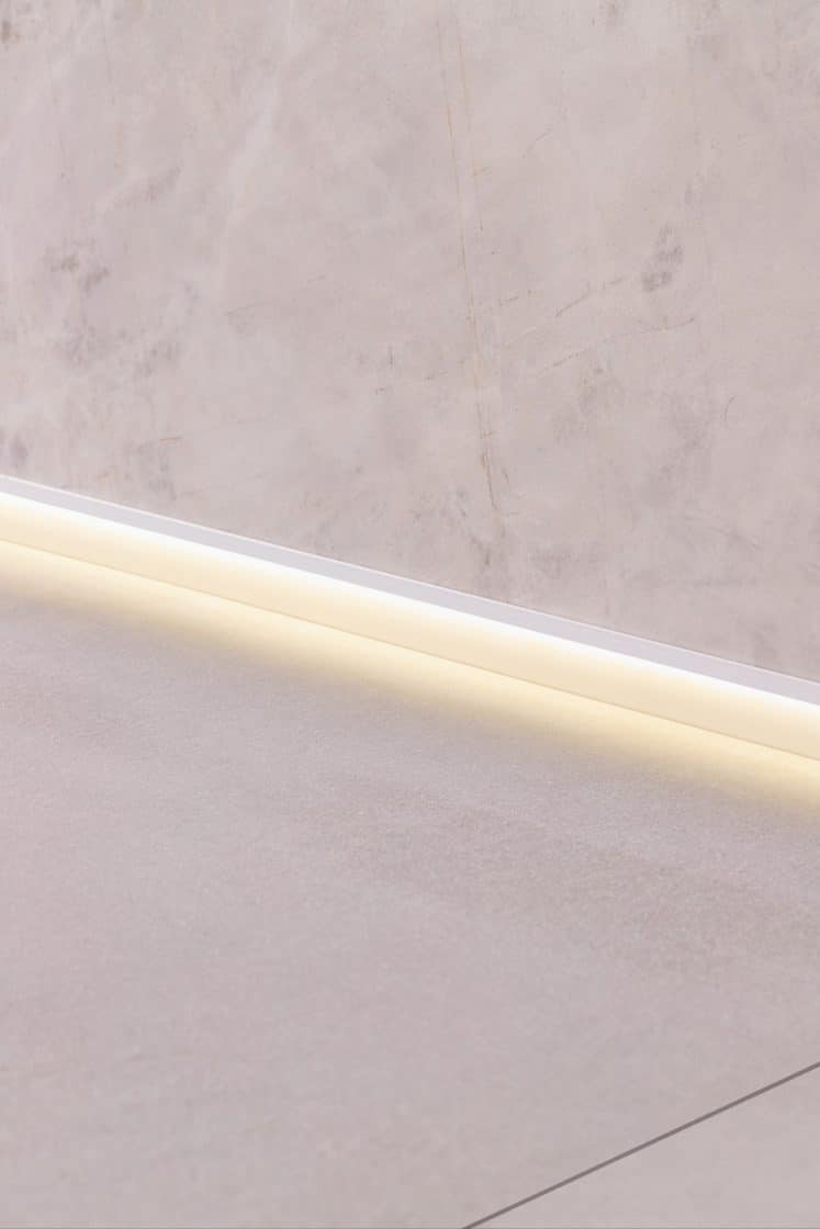 Ambiente com parede acinzentada, rodapé invertido preto e uma mesa lateral pequena com um vaso decorativo em cima (Projeto: Portobello)