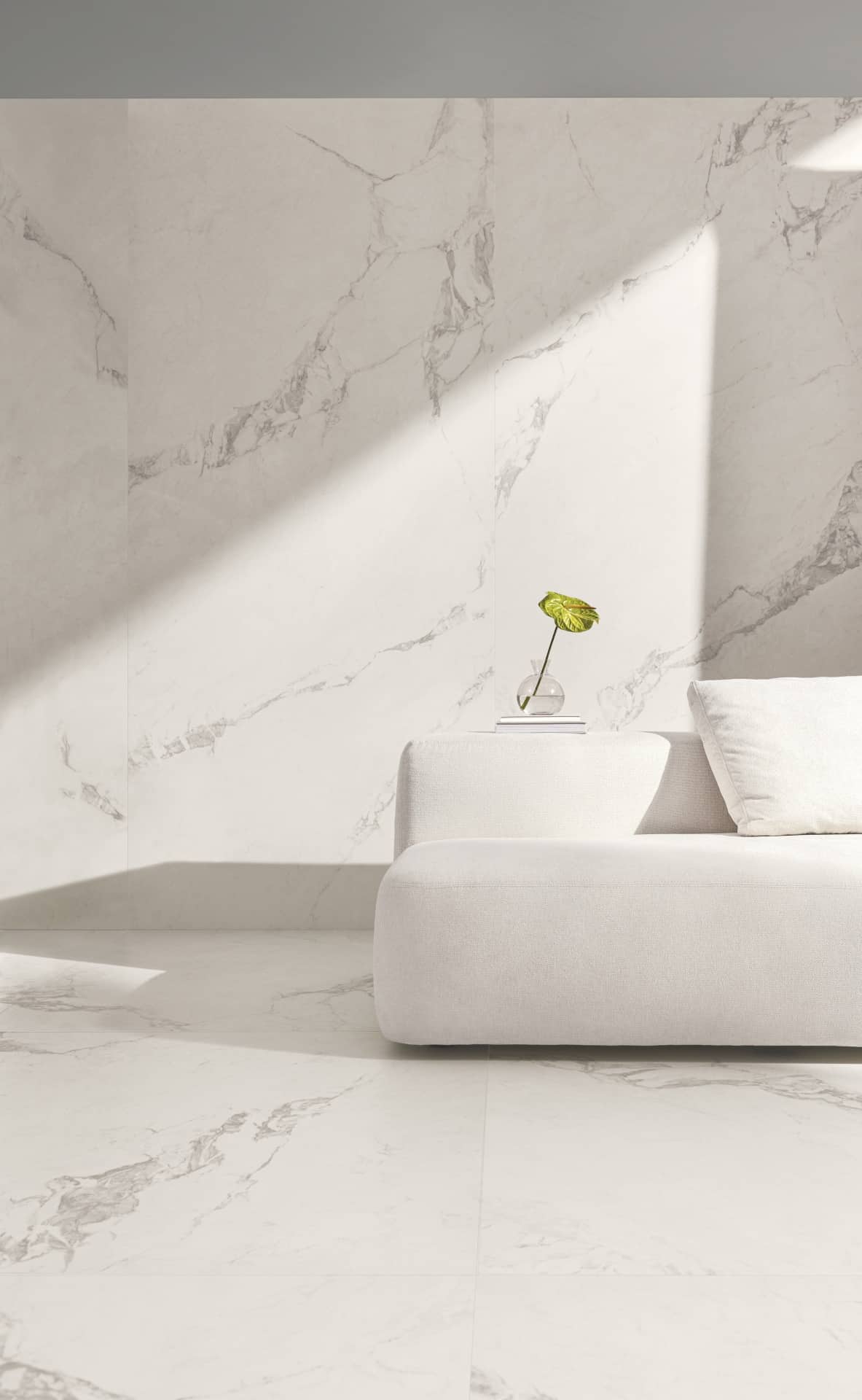 Detalhe de sala de estar com piso e parede de porcelanato. Há também um sofá branco e um vaso com planta.