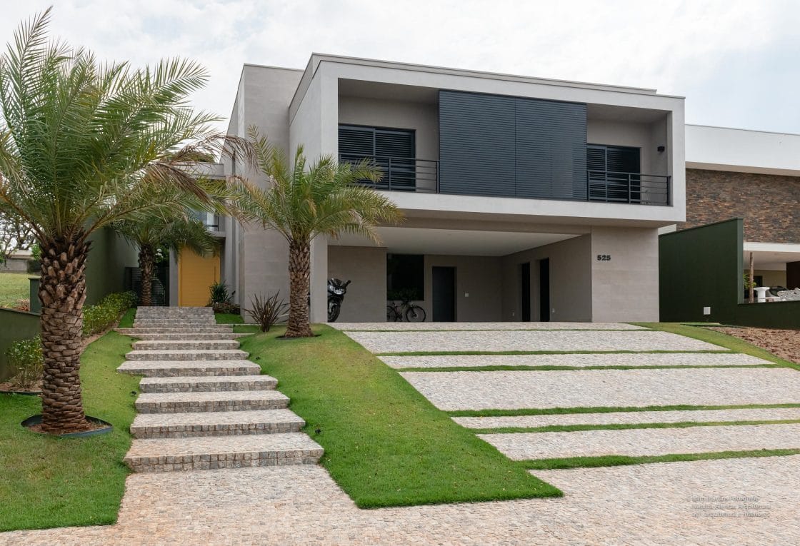 Casa com linhas e cores modernas. Na frente se destaca uma árvore e a rampa de garagem (Projeto: Ivanilza de Alencar)
