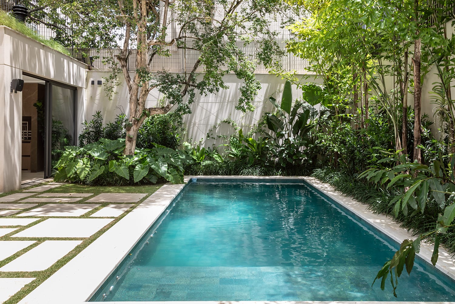 Jardim com piscina e sauna, piso em porcelanato deck de madeira com jardim nas laterais da piscina. A escolha do piso ideal, com resistência ao escorregamento e de fácil manutenção, é fundamental para garantir segurança e praticidade (Projeto: IN CASA Arquitetura + Design / Foto: Mak Cézar)