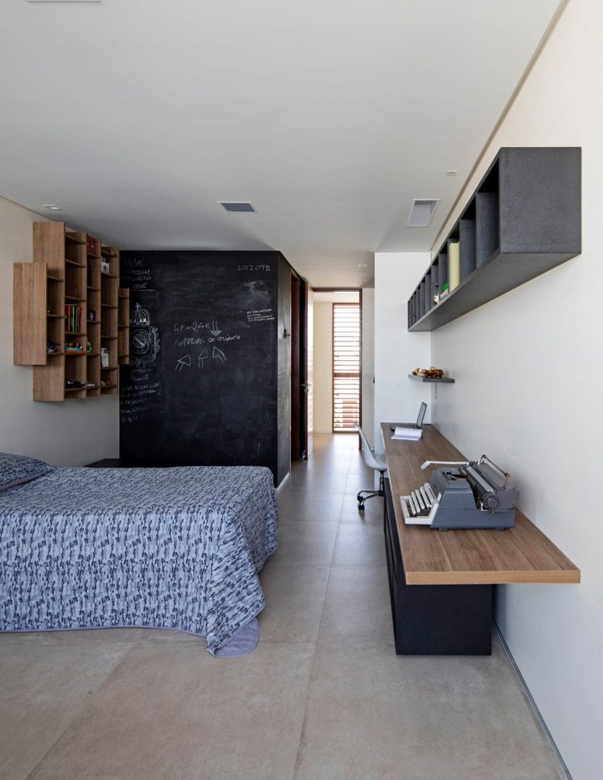 Quarto home office com cama de solteiro, bancada de madeira e área de trabalho (Projeto: Martins Lucena Arquitetos)