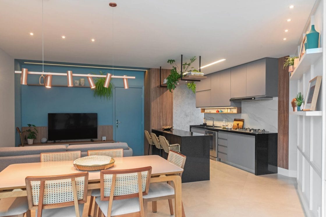 Cozinha, sala de estar e sala de jantar integradas com diversos móveis e parede do fundo azul (Projeto: Tatiana Pradal / Foto: Giovana Gonçalves)