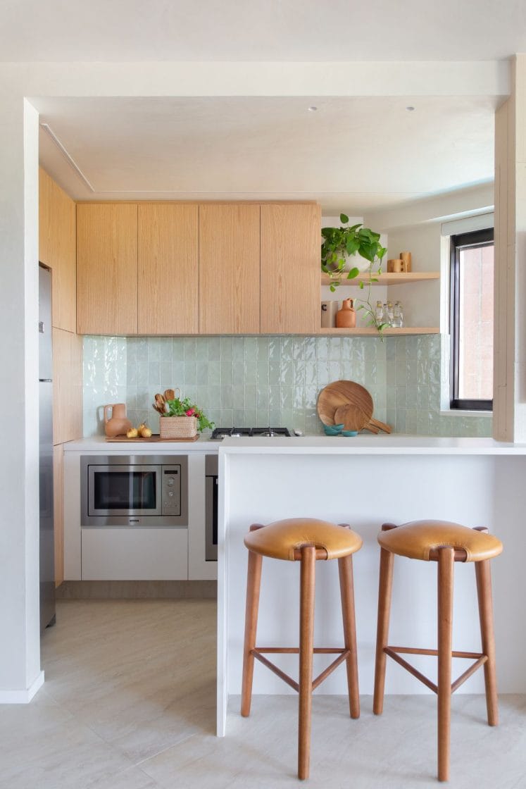 Cozinha bem iluminada com armários de madeira, revestimento verde-claro, bancada e banquetas de madeira (Projeto: Arquiteto David Oliveira / Foto: @RaianaMedina.FotoArq)