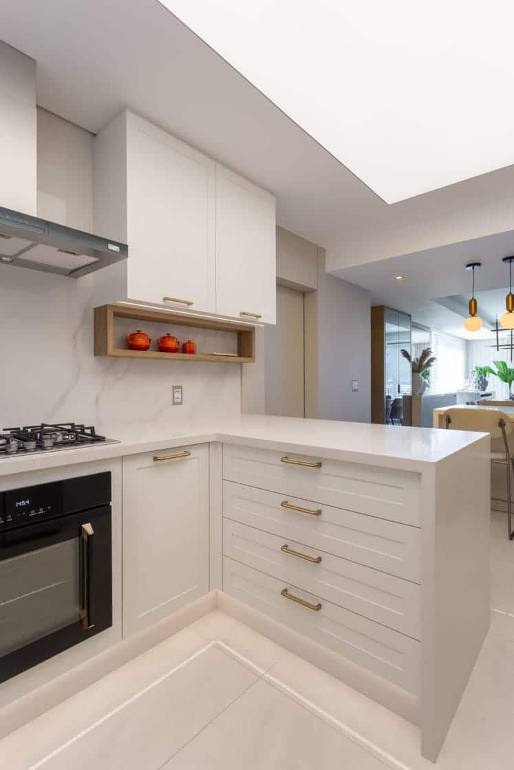 Cozinha em tons neutros com bancada com armários e puxadores dourados.