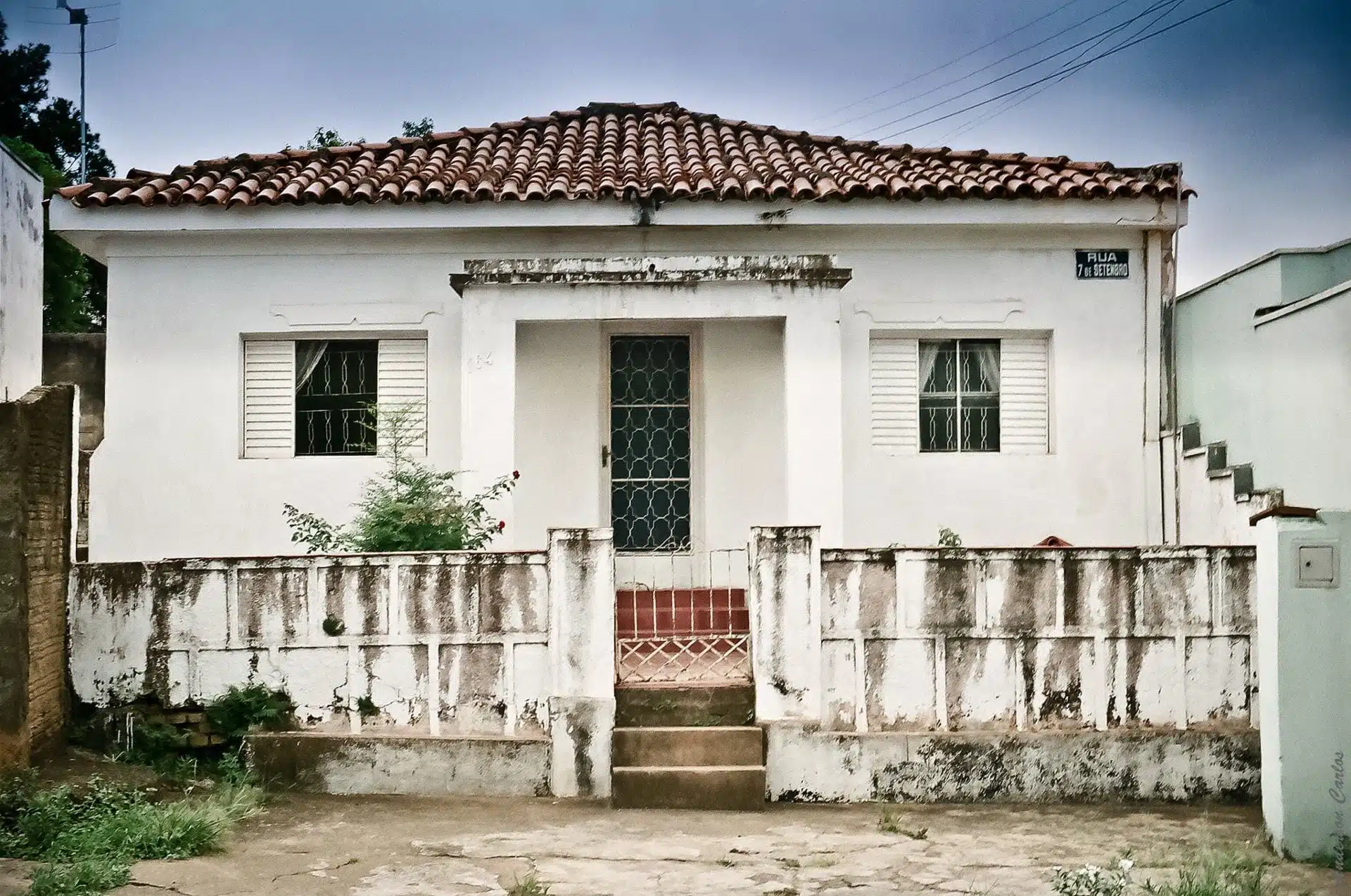 Casa de um pavimento na cor branca, com muro baixo e telhado colonial, ideal para reforma.
