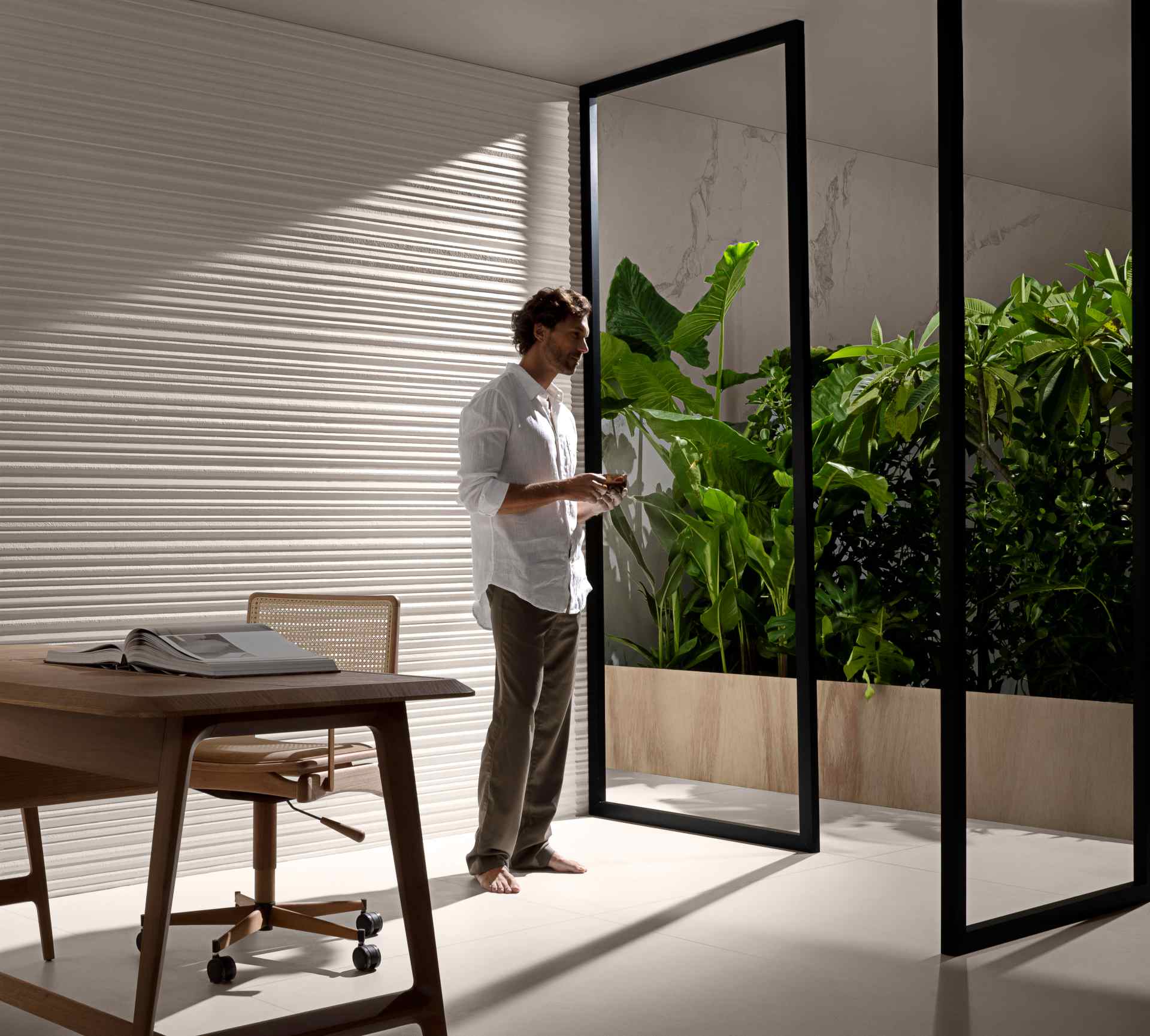 Detalhe de home office com piso e parede em tom cru; há uma porta de vidro que leva a uma área verde