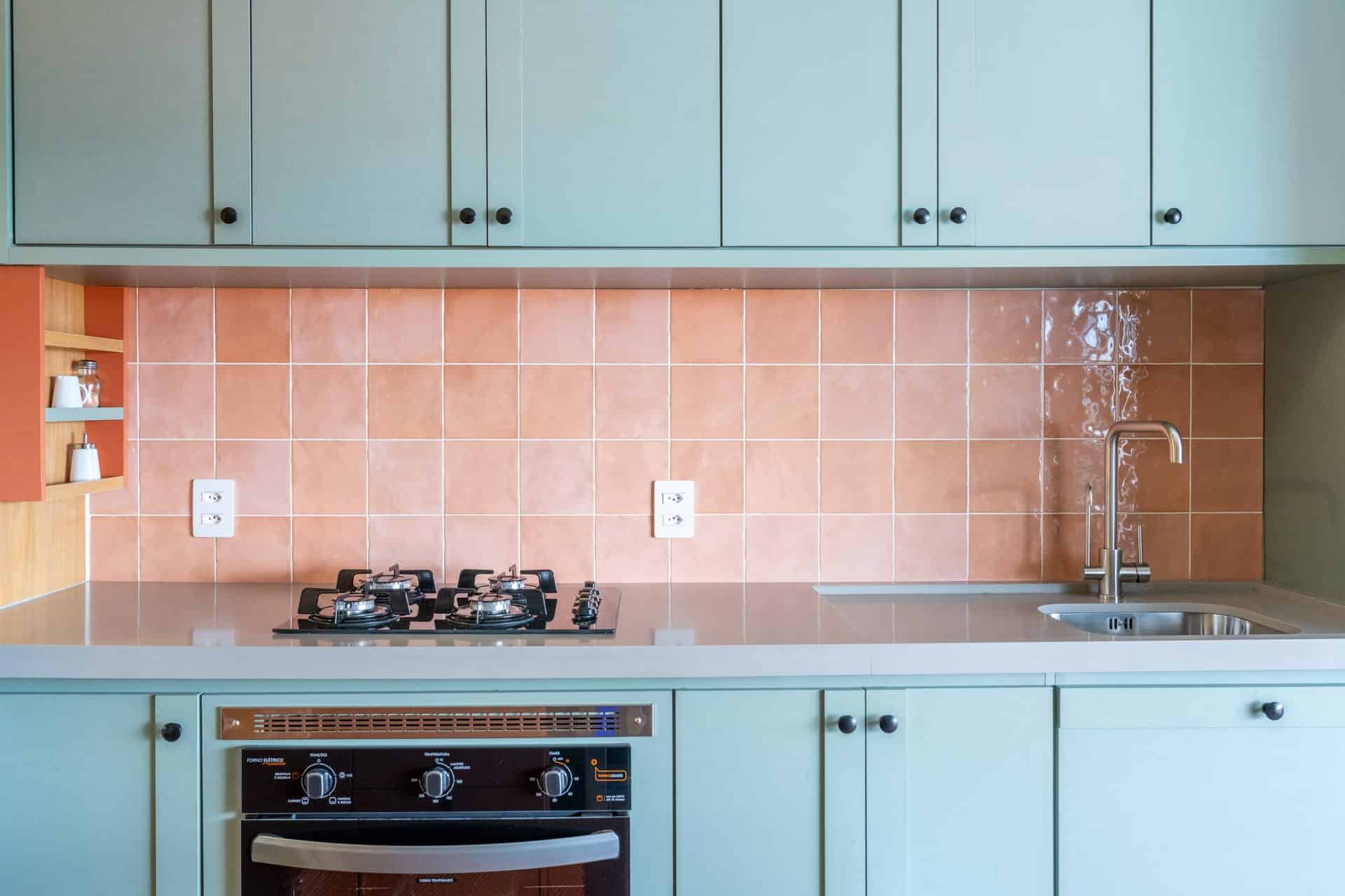 Cozinha com armários azuis e azulejos rosados.