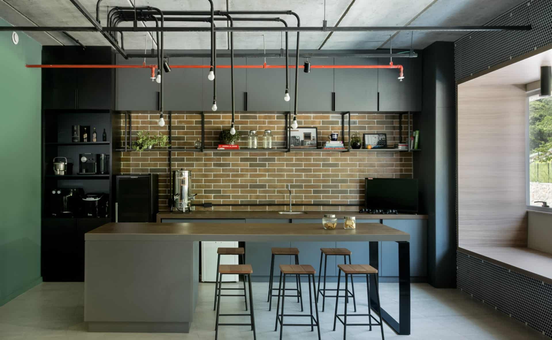 Cozinha estilo industrial com armários pretos, ilha em madeira, banquetas, luminária e revestimento que lembra tijolinhos na parede.