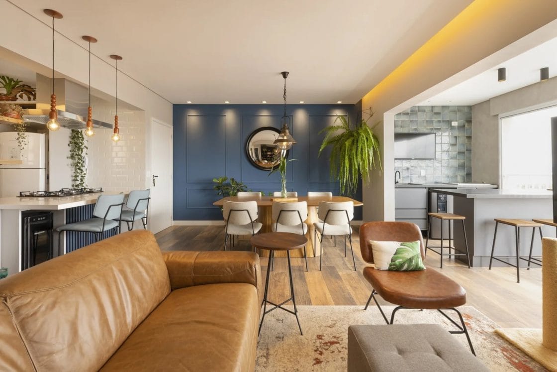Sala de estar com parede azul-marinho em destaque, com boiseries. Ambiente integrado ainda tem mesa de jantar, sofá e cadeiras.