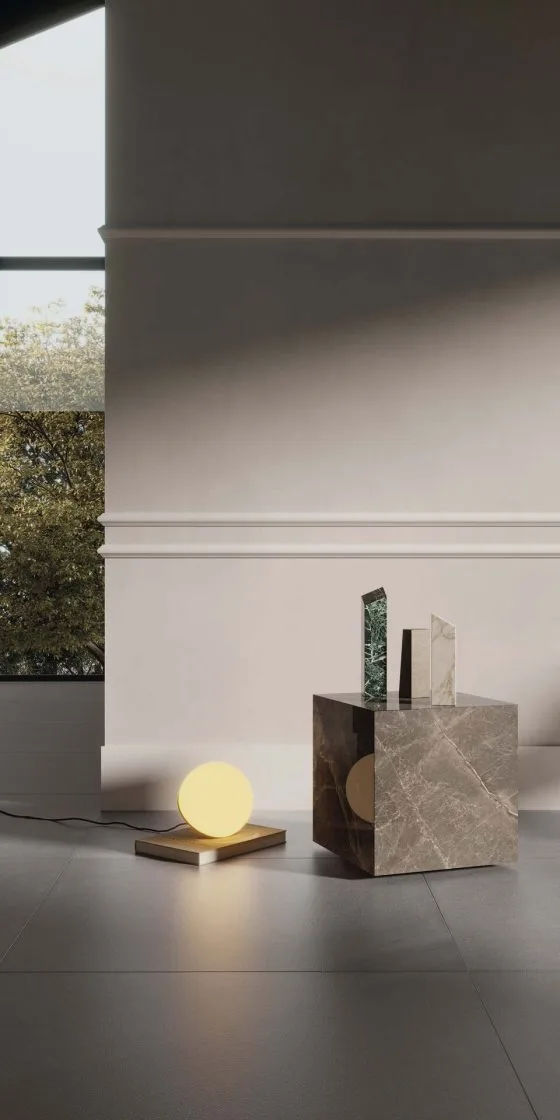 Parede com tom acinzentado e rodameio em branco. À frente, temos uma mesinha quadrada com objetos de decoração e uma luminária no piso.